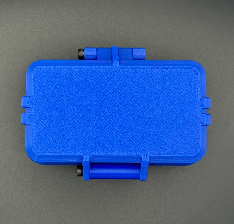 May include: A rectangular blue storage case with a textured surface and rounded corners. The case features a hinged lid mechanism with visible black metal screws on the side hinges, providing a secure closure for the container.