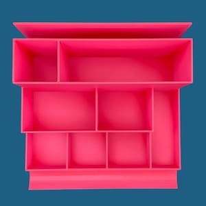 Może przedstawiać: Różowy plastikowy organizer z wieloma przegródkami. Organizer ma wielopoziomowy design z górną półką i dwiema dolnymi półkami.