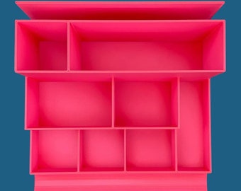 Op de afbeelding: Een felroze bureau-organizer met een getrapt ontwerp en meerdere rechthoekige vakken van verschillende groottes. De structuur bevat één lang bovenvak, twee middelste vakken en vier kleinere onderste vakken voor opslag.
