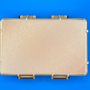 May include: A rectangular, tan-colored protective storage case with a textured, pebbled surface finish. The case features two prominent hinges along the top edge and two matching latch mechanisms along the bottom edge, all in a solid tan color.