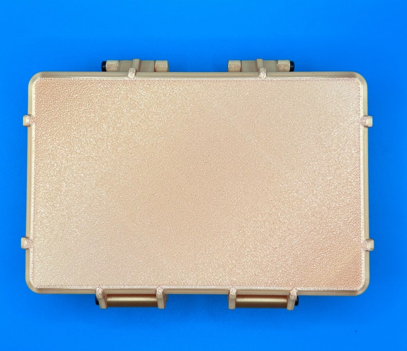 May include: A rectangular, tan-colored protective storage case with a textured, pebbled surface finish. The case features two prominent hinges along the top edge and two matching latch mechanisms along the bottom edge, all in a solid tan color.