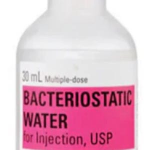 May include: A 30 mL multiple-dose vial of Bacteriostatic Water for Injection, USP, manufactured by Hospira, Inc., Lake Forest, IL. The clear glass vial features a bright pink label with black text and a pink plastic flip-top cap.