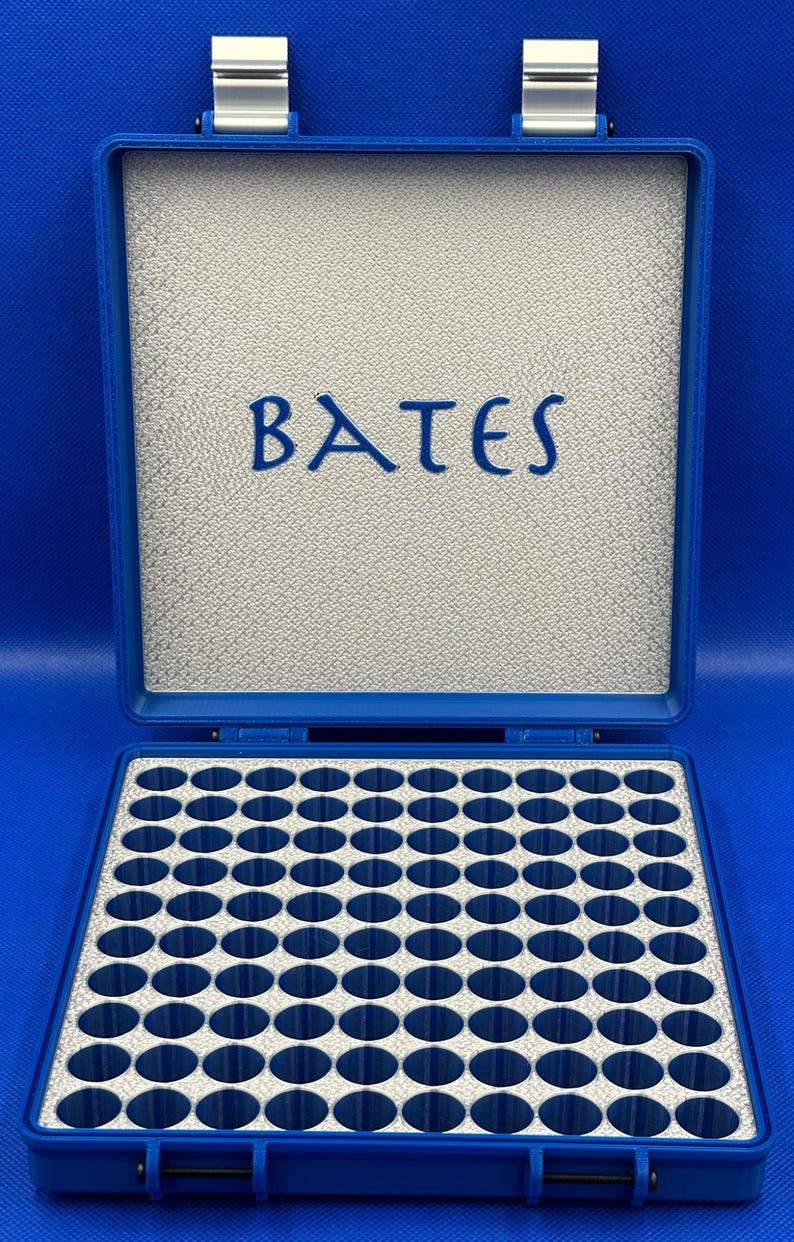 K&ouml;nnte beinhalten: Eine blaue Plastikbox mit grauem Innenraum und einem Raster aus 64 runden F&auml;chern. Die Box hat einen silbernen Verschluss und das Wort "BATES" ist auf dem Deckel aufgedruckt.