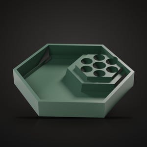 Pu&ograve; includere: Un vassoio esagonale color verde salvia caratterizzato da una sezione esagonale pi&ugrave; piccola e rialzata con sette fori circolari. Il vassoio presenta una finitura opaca liscia e un design geometrico con bordi netti e una zona profonda.