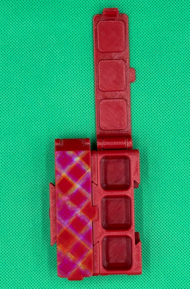 Puede incluir: Una caja de pl&aacute;stico roja con un patr&oacute;n a cuadros en la parte delantera y cuatro compartimentos en la parte posterior. La caja est&aacute; dise&ntilde;ada para guardar objetos peque&ntilde;os, como botes de pintura u otros materiales de arte.