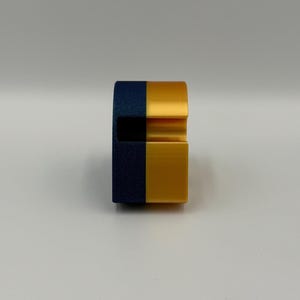 May include: A two-tone, geometric object with a navy blue and gold color scheme. The object has a rectangular base and a curved top with a groove. The design is modern and minimalist.