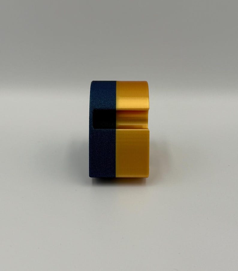 May include: A two-tone, geometric object with a navy blue and gold color scheme. The object has a rectangular base and a curved top with a groove. The design is modern and minimalist.