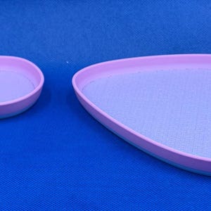 May include: Two pastel purple oval-shaped trays with a light blue rim. The smaller tray is on the left and the larger tray is on the right.