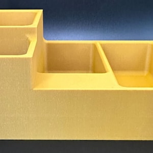 Op de afbeelding: Een gele plastic organizer met vier vakken. De organizer heeft een verhoogd gedeelte met twee kleinere vakken.