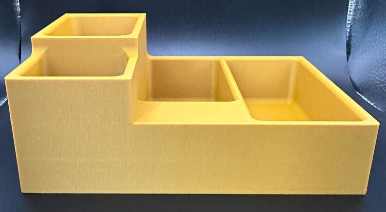Op de afbeelding: Een gele plastic organizer met vier vakken. De organizer heeft een verhoogd gedeelte met twee kleinere vakken.