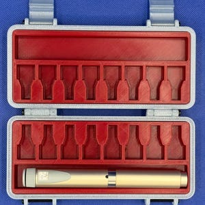 May include: A rectangular storage case with a light gray exterior and a red interior featuring molded slots for small items. One gold-colored cylindrical pen-like tool with a white dial and a small digital display is placed in the bottom row.