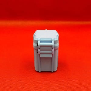 May include: A light blue, rectangular, hard-shell storage case with a textured top surface and a vertical latch mechanism on the side. The container features a solid, matte finish and a structured, boxy design with rounded corners.