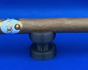 May include: A brown cigar with a white and gold label that reads "OLIVA" is resting on a black cigar holder.