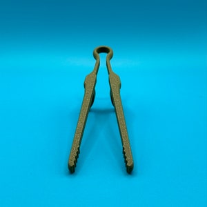 May include: A pair of olive green kitchen tongs with a textured, matte finish. The tongs feature a looped handle at the top and two long, straight arms that taper toward the bottom, ending in small, serrated gripping edges for handling food.