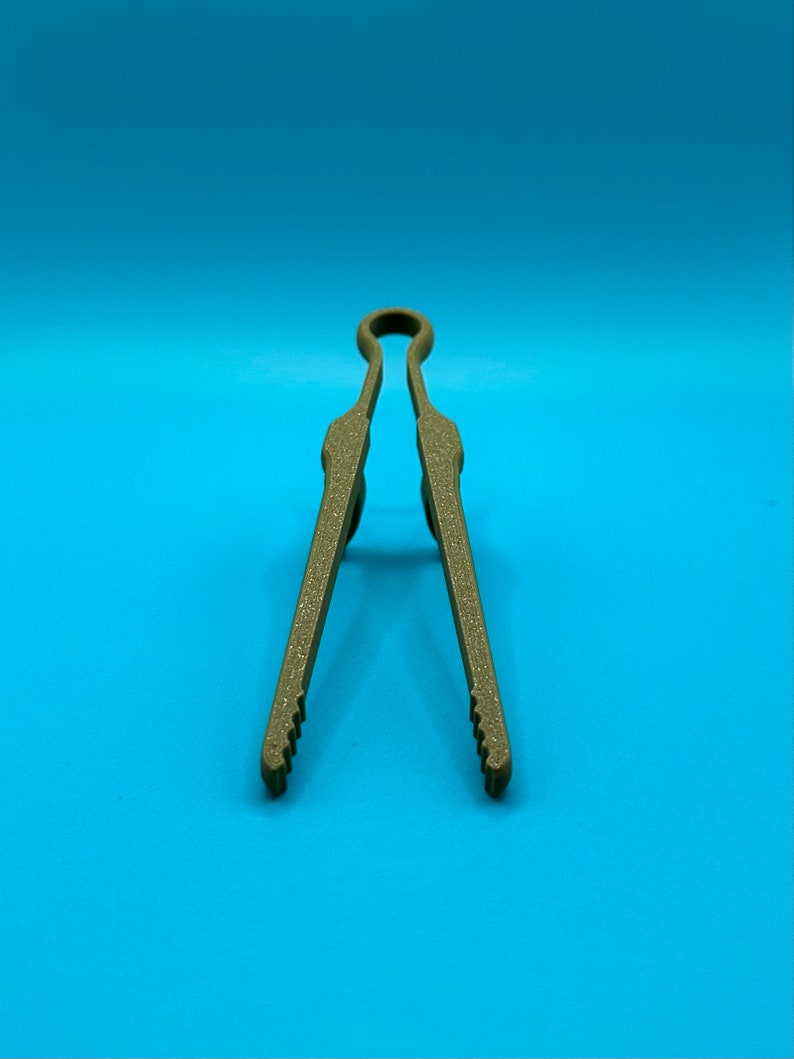 May include: A pair of olive green kitchen tongs with a textured, matte finish. The tongs feature a looped handle at the top and two long, straight arms that taper toward the bottom, ending in small, serrated gripping edges for handling food.