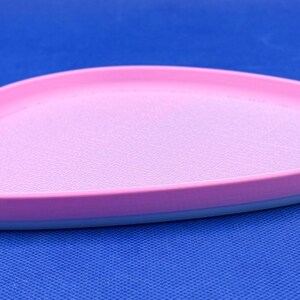May include: A pink and blue oval-shaped tray with a textured surface. The tray is made of plastic and has a smooth, rounded edge.
