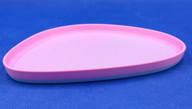 May include: A pink and blue oval-shaped tray with a textured surface. The tray is made of plastic and has a smooth, rounded edge.