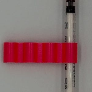 May include: A medical syringe with a clear barrel and black markings, capped with orange plastic. A bright pink, ridged plastic piece is attached to the syringe. The syringe is designed for precise measurements.