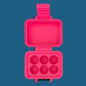 May include: A bright neon pink rectangular storage case with a hinged lid. The interior of the bottom section features six circular indentations arranged in two rows of three, while the top section is an open, empty rectangular compartment.