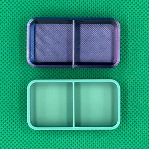 May include: Two rectangular, divided containers. The top container is a gradient of purple and blue, with a crosshatch pattern. The bottom container is a solid light green color. Both containers have rounded corners.