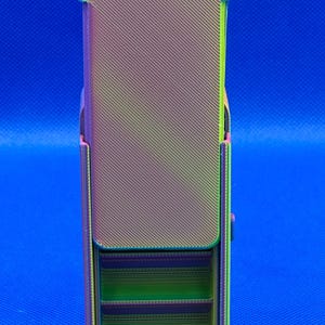 May include: A rectangular, 3D-printed storage container featuring a gradient color scheme that transitions from purple to green and yellow. The exterior has a diagonal ribbed texture, and the front section reveals internal horizontal shelves.