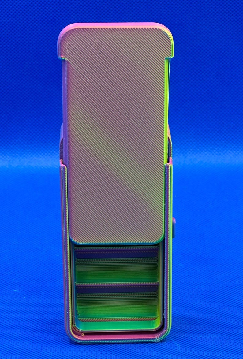 May include: A rectangular, 3D-printed storage container featuring a gradient color scheme that transitions from purple to green and yellow. The exterior has a diagonal ribbed texture, and the front section reveals internal horizontal shelves.