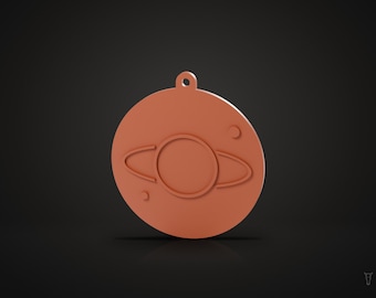 May include: A circular, terracotta-coloured pendant featuring a raised relief design of a planet with rings and two smaller circular celestial bodies. The pendant has a small loop at the top for attachment, providing a flat, matte surface.
