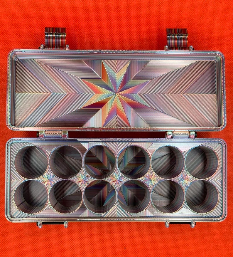 May include: A rectangular metal storage case with an open lid, featuring a multi-coloured iridescent finish and a geometric star pattern. The base contains ten circular cutouts arranged in two rows, with matching iridescent star motifs.