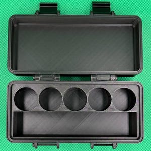 Puede incluir: Un estuche de almacenamiento rectangular negro con tapa abatible y dos cierres de seguridad. El interior cuenta con cinco aberturas circulares dispuestas en fila y un compartimento rectangular para organizar objetos peque&ntilde;os.
