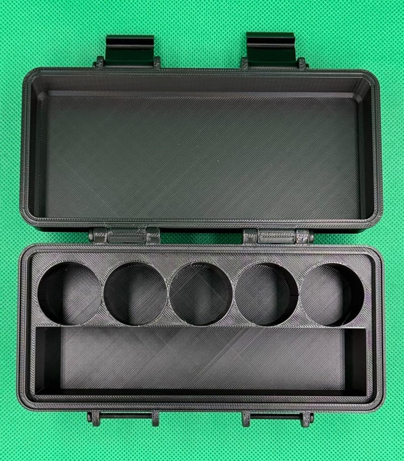 Puede incluir: Un estuche de almacenamiento rectangular negro con tapa abatible y dos cierres de seguridad. El interior cuenta con cinco aberturas circulares dispuestas en fila y un compartimento rectangular para organizar objetos peque&ntilde;os.