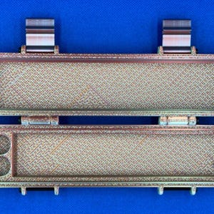 May include: A two-piece, brown and gold, rectangular storage case with a textured surface. The case has two compartments, one with two small circular holes and the other with a larger rectangular space.