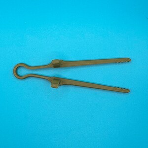 May include: A pair of olive green kitchen tongs featuring a single-piece construction with a looped handle, two raised rectangular grips along the center of each arm, and serrated edges at the tips for improved gripping of food items.