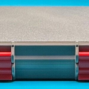 May include: A gray plastic storage case with two red latches. The case has a textured surface and is closed.