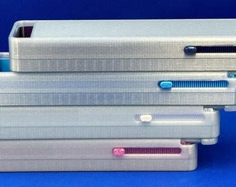 May include: A stack of four rectangular, silver-toned plastic cases, each featuring a sliding mechanism on the side. The sliders are colored dark blue, light blue, white, and pink, matching the interior accents visible at the open ends.