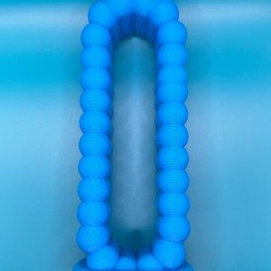 May include: A blue 3D printed object shaped like the letter "O" with a rounded top and bottom. The object is made up of many small spheres.