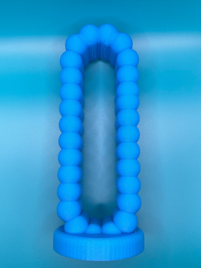 May include: A blue 3D printed object shaped like the letter "O" with a rounded top and bottom. The object is made up of many small spheres.