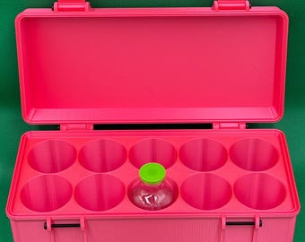 May include: A bright pink rectangular storage case with an open lid and ten circular compartments. One small clear glass vial with a vibrant lime green cap is placed inside one of the circular slots. The case features two black hinges on the front.
