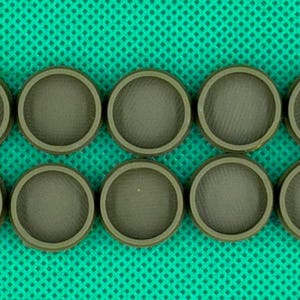 May include: Ten circular, olive-green plastic caps arranged in two rows of five. Each cap features a raised outer rim and a recessed, textured center surface with a fine, cross-hatched pattern visible across the flat interior base.