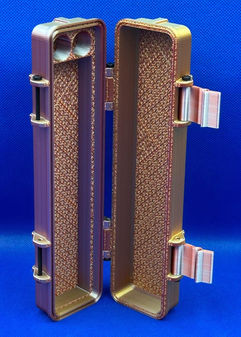 May include: A small, rectangular, brown, 3D printed case with a hinged lid. The case is open, revealing an empty interior. The case has a textured surface and a small hole on the inside of the lid.