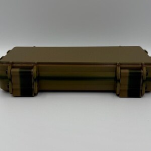 May include: A rectangular, tan-colored hard-shell storage case with a smooth, flat top surface. The case features two dark brown, vertical locking latches on the front edge, designed to secure the lid firmly to the base of the container.