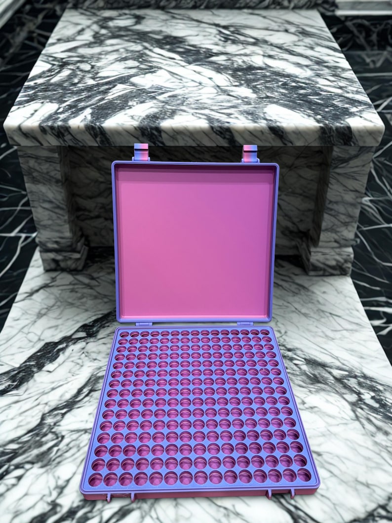 May include: An open, rectangular, pink and purple case with a grid of circular holes. The case is on a marble surface. The case has a purple frame and a pink interior. The case is open, revealing a tray with many circular holes.