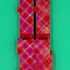 Puede incluir: Dos piezas de pl&aacute;stico rojo con un patr&oacute;n a cuadros. Las piezas est&aacute;n conectadas por una bisagra.