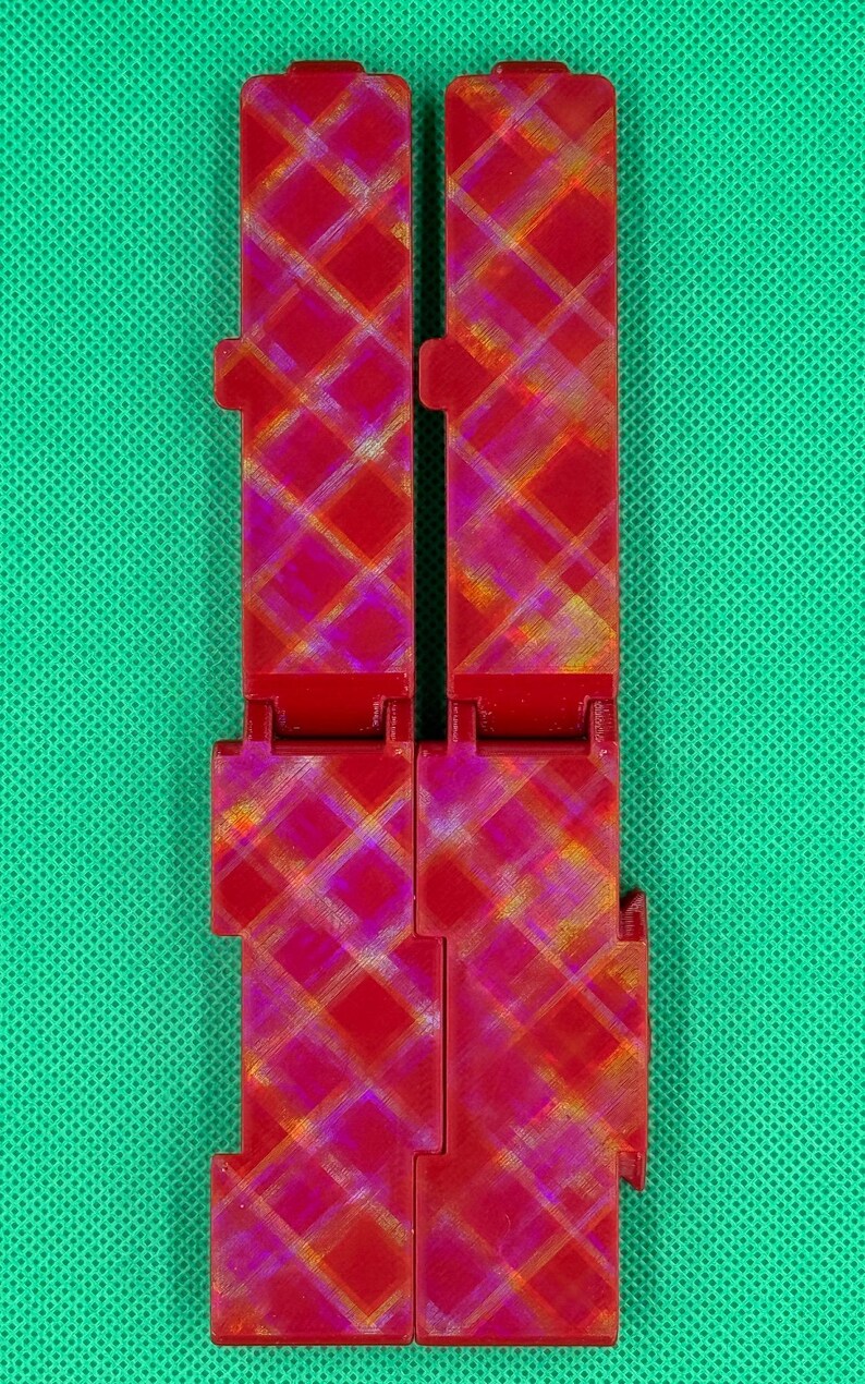 Puede incluir: Dos piezas de pl&aacute;stico rojo con un patr&oacute;n a cuadros. Las piezas est&aacute;n conectadas por una bisagra.
