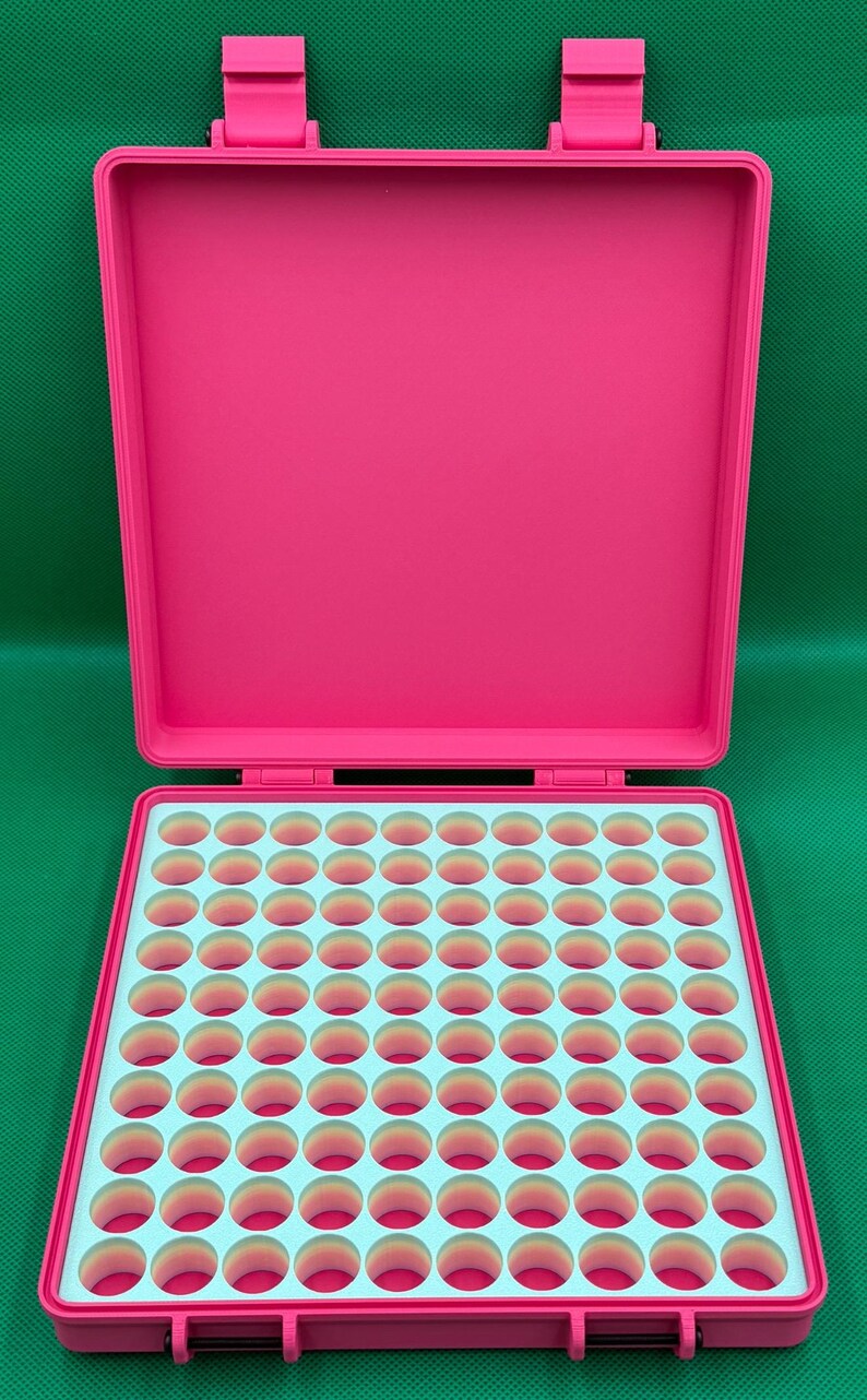 May include: A bright pink plastic storage case with a hinged lid and two latches. The interior features a light blue grid insert with one hundred circular cutouts, each revealing a gradient of pink and orange colors at the base.