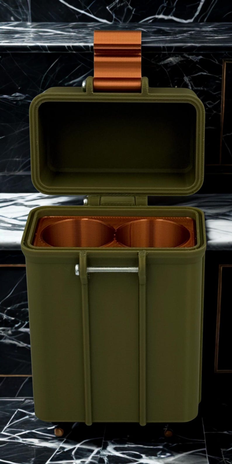 May include: An olive green rectangular storage container with an open hinged lid. The interior features two circular copper-colored compartments. A metallic silver pin secures the front, and a copper-colored strap is attached to the top lid.