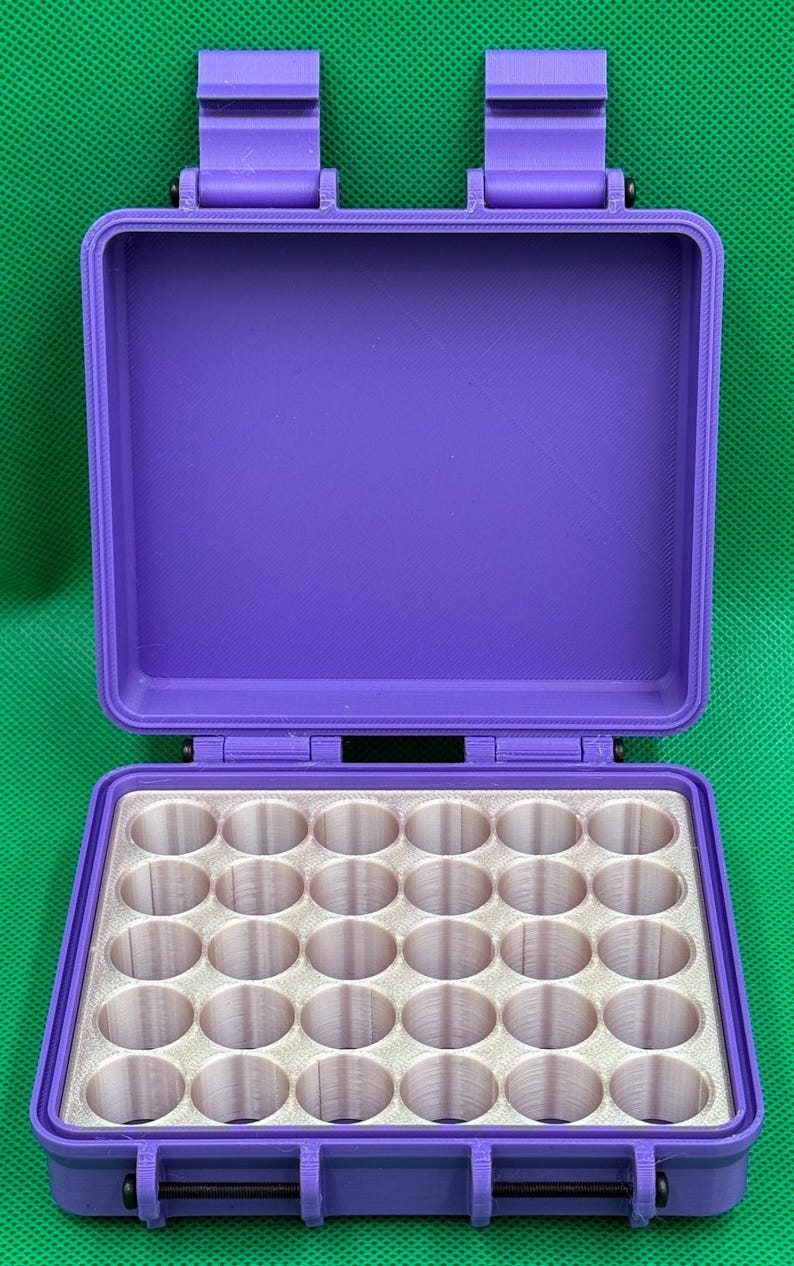 May include: A purple rectangular storage case with two top latches and a hinged lid. The interior features a white insert with a grid of thirty-two circular cylindrical compartments arranged in four rows of eight for organizing small items.
