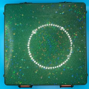 May include: A square, dark green storage case with a textured surface featuring embedded holographic star-shaped glitter. A circular arrangement of small, clear, reflective beads is centred on the lid of the case.