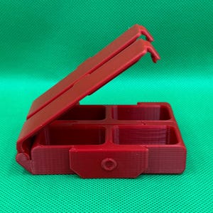 Puede incluir: Una caja de pl&aacute;stico roja con cuatro compartimentos, con bisagras en un lado y que se abre como una concha. La caja est&aacute; cerrada y la tapa est&aacute; abierta.