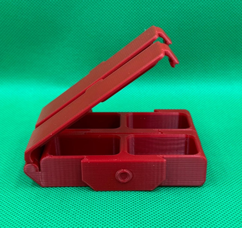 Puede incluir: Una caja de pl&aacute;stico roja con cuatro compartimentos, con bisagras en un lado y que se abre como una concha. La caja est&aacute; cerrada y la tapa est&aacute; abierta.