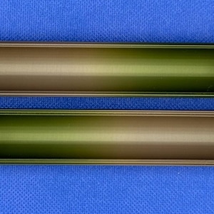May include: Two metal tubes with a gradient color scheme, transitioning from a dark brown to a light green. The tubes are hollow and have a slightly rounded edge.